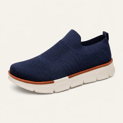 Navy XE5813 knit slip-on shoe with a brown welt and cream segmented sole on a warm off-white background.